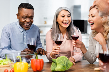 selective focus of smiling multicultural friends talking and holding wine glasses in kitchen
