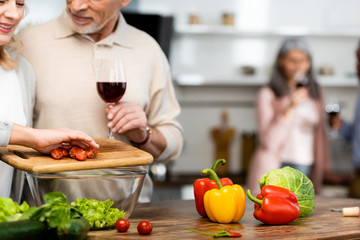 cropped view of smiling woman adding cut cherry tomatoes to bowl and man holding wine glass
