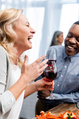 selective focus of smiling woman and african american man talking and holding wine glasses
