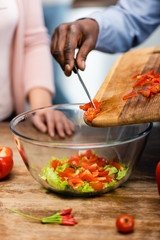 cropped view of african american man adding cut bell pepper to bowl and woman standing near him