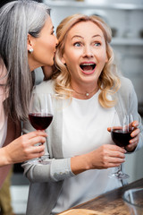 asian woman telling secret to shocked friend with wine glass
