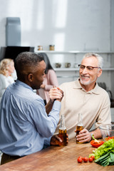 Fototapeta na wymiar african american man holding hands and talking with smiling friend in kitchen