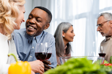 selective focus of multicultural friends talking and holding wine glasses