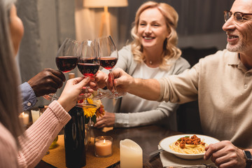 selective focus of smiling multicultural friends clinking during dinner