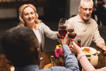 selective focus of smiling multicultural friends clinking during dinner