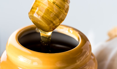 A macro close up of a honey dipper with honey dripping off into a honey pot. 
