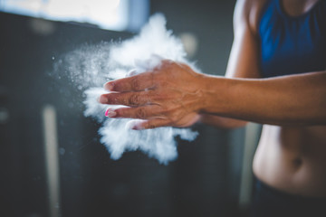 Obraz na płótnie Canvas Female fitness model clapping hands with talcum powder in a gym before weight training