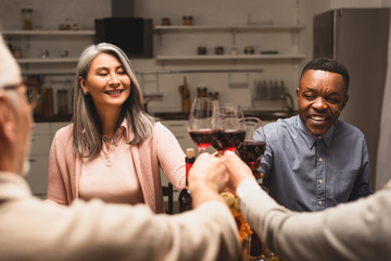 selective focus of smiling multicultural friends clinking during dinner