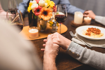 cropped view of man holding hand of friend and praying during dinner
