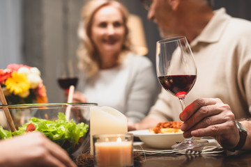 selective focus of man holding wine glass and talking with smiling woman during dinner