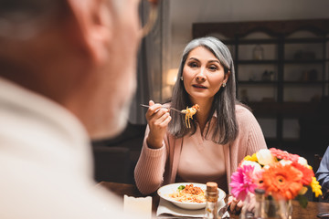 selective focus of asain woman eating pasta and looking at friend during dinner