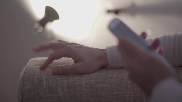Stress of modern life: close-up of the woman's hands tapping nervously with her fingers on the sofa waiting for a message on her smartphone in a modern ambience of soft light, no grade slog