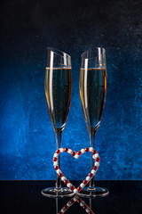 Two glasses with champagne on a black mirror surface. Heart for St. Valentine. Blue background Concrete wall. Black glass. Crystal glass