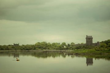 Fototapeta na wymiar View of the Dunguaire Castle, Galway Bay in Kinvara, Ireland. Beautiful landscape with with the bay and the Atlantic Ocean and a green forest. Reflections on the water.