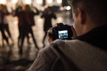 Young boy recording a video with the reflex camera to a group of people at night