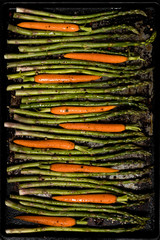 A top down view of a baking tray with asparagus and carrots ready for baking.