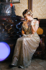 a woman in a gold dress sits on a chair in long gloves with a diodema, a wave looks down on her...