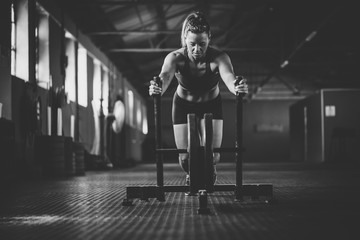 Female fitness model pushing a sled in a cross fit gym.