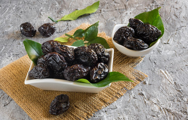 bowl of sweet dried plums with lemon leaves on rustic stucco background