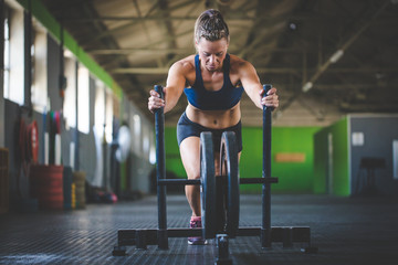 Female fitness model pushing a sled in a cross fit gym. - Powered by Adobe
