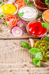 Set of sauces in small bowls - ketchup, mayonnaise, mustard, bbq sauce, pesto, classic burger sauce, with spices and herbs in. Wooden background copy space top view