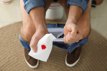 Man holding toilet paper with blood stain in rest room, closeup. Hemorrhoid concept - obrazy, fototapety, plakaty