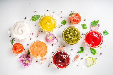 Set of sauces in small bowls - ketchup, mayonnaise, mustard, bbq sauce, pesto, classic burger sauce, with spices and herbs in. White background copy space top view - obrazy, fototapety, plakaty