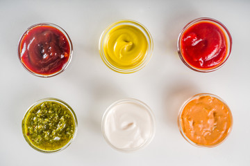 Set of sauces in small bowls - ketchup, mayonnaise, mustard, bbq sauce, pesto, classic burger sauce, with spices and herbs in. White background copy space top view