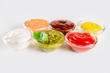 Set of sauces in small bowls - ketchup, mayonnaise, mustard, bbq sauce, pesto, classic burger sauce, with spices and herbs in. White background copy space top view