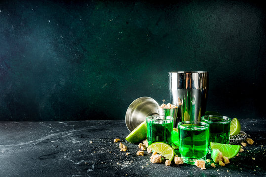 Strong alcohol. Absinthe with sugar, ice cubes and lime slices, Three shot glasses with absinthe. Dark stone background copy space