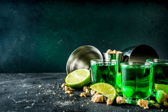 Strong alcohol. Absinthe with sugar, ice cubes and lime slices, Three shot glasses with absinthe. Dark stone background copy space