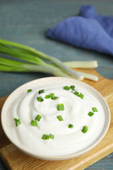 Fresh sour cream with onion on wooden board, closeup