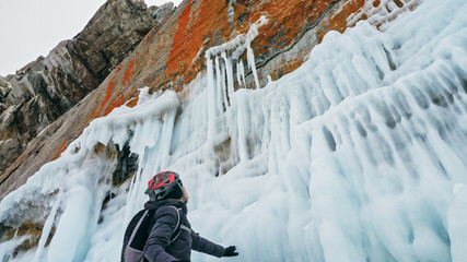 Man is riding bicycle near ice grotto. Rock with ice caves icicles. Teenage is dressed in black...