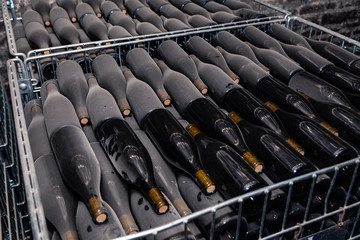 Fototapeta premium Ancient wine bottles resting, aging, dusting in underground cellar in rows. Concept winery vault with rare wines, exclusive collection. Stacks of wine bottles laying flat in racks in old cave