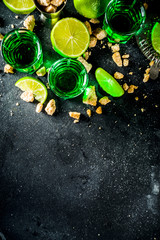 Fototapeta na wymiar Strong alcohol. Absinthe with sugar, ice cubes and lime slices, Three shot glasses with absinthe. Dark stone background copy space