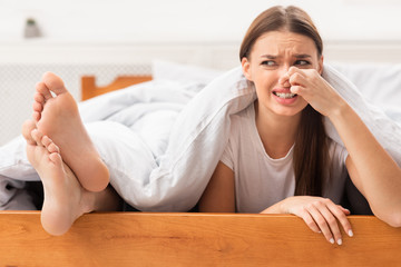 Girlfriend Pinching Nose Lying Near Boyfriend's Smelly Feet In Bed - obrazy, fototapety, plakaty