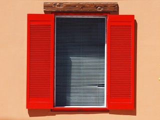 Vintage window on the wall with red shutters and white blinds closeup