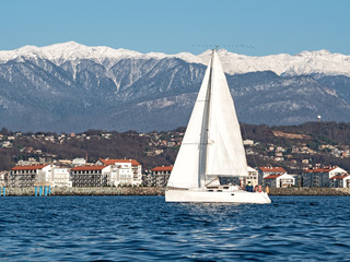 White sailing yacht on sea water at coast and mountains background. Imeretian resort in Adler (Sochi, Russia)