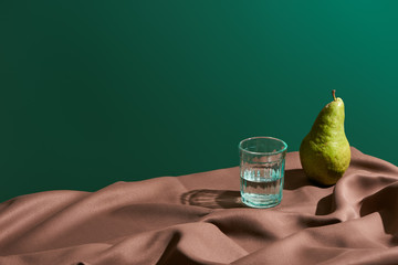 classic still life with pear and water in glass on table with brown tablecloth isolated on green