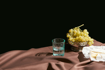 classic still life with Camembert cheese, grape and water in glass on table with brown tablecloth isolated on black