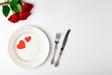 Fototapeta na wymiar Valentines day dinner with festive table setting, red roses, tape, hearts, ceramic plate, vintage silverware on white background. Top view, space for text, copy space, birthday greeting, anniversary