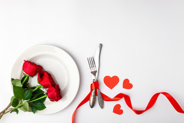 Valentines day dinner with festive table setting, red roses, tape, hearts, ceramic plate, vintage silverware on white background. Top view, space for text, copy space, birthday greeting, anniversary