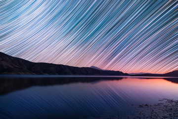 Night landscape. Beautiful lake and mountains at the night. The colorful star trails on the sky....