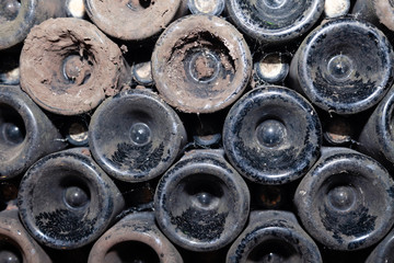 Closeup pattern from bottom of old dark dusty wine bottles in rows in cellar, basement, wine warehouse, winery. Concept vault with old rare wines, exclusive collection rare bottle. Mosaic background