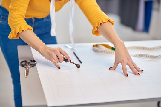 Close up of dedicated caucasian seamstress cutting seam pattern with rotary cutter.