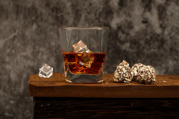Whiskey with ice or brandy in a glass with truffles on a wooden table and a gray background....