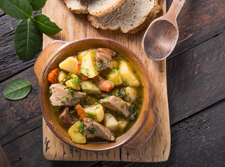 Irish dinner. Beef meat stewed with potatoes, carrots and soda bread on wooden background, top view, copy space. Homemade winter comfort food - slow cooked