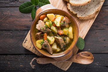 Irish dinner. Beef meat stewed with potatoes, carrots and soda bread on wooden background, top view, copy space. Homemade winter comfort food - slow cooked