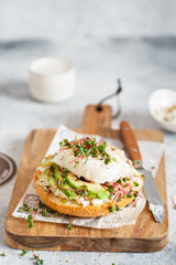 Poached egg with avocado, ricotta cheese and radish sprouts on burger bun. Healthy sandwich with bread, fresh avocado, poached egg and cheese garnished with radish microgreens. Healthy eating