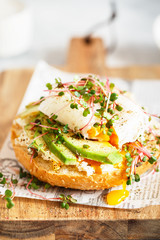 Poached egg with avocado, ricotta cheese and radish sprouts on burger bun. Healthy sandwich with bread, fresh avocado, poached egg and cheese garnished with radish microgreens. Healthy eating